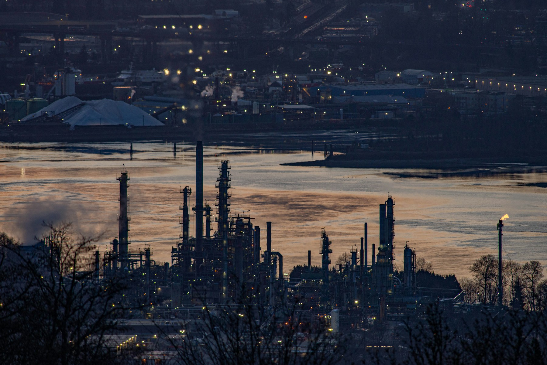 Illuminated refinery beside the water at dusk, illustrative industry photography
